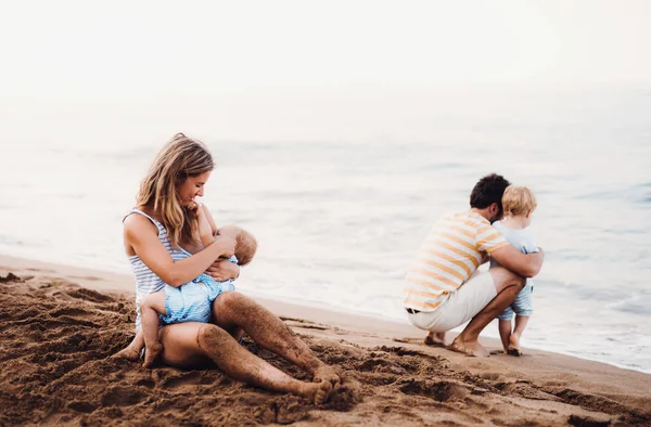 Giovane famiglia con due bambini piccoli in spiaggia in vacanza estiva . — Foto Stock