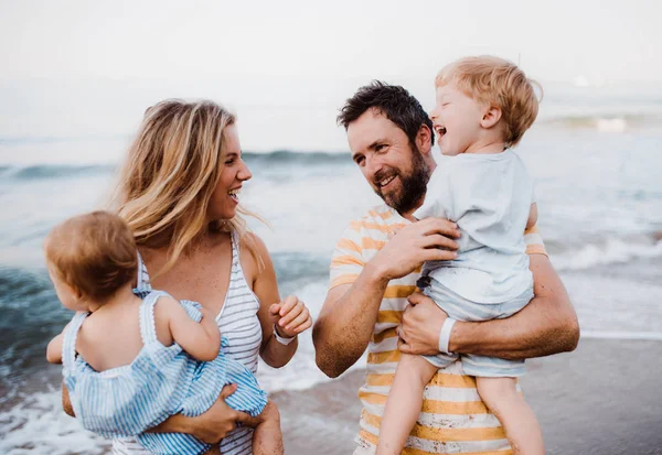 En ung familj med två småbarn barn stående på stranden på sommarsemester. — Stockfoto