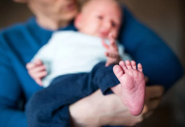 Un père tenant un nouveau-né à la maison, pieds nus au premier plan . — Photo