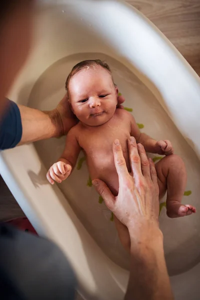 Vista superior de los padres irreconocibles que dan a un bebé recién nacido un baño en casa . — Foto de Stock