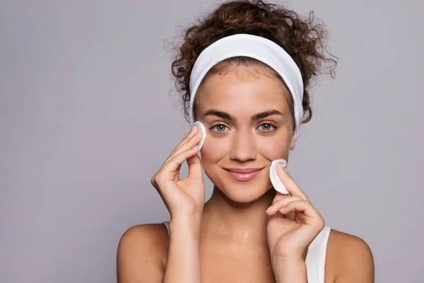 Retrato de una joven limpiando la cara en un estudio, belleza y cuidado de la piel . — Foto de Stock