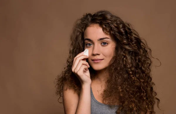 Portret van een jonge vrouw die make-up aanbrengt in een studio tegen bruine achtergrond. — Stockfoto