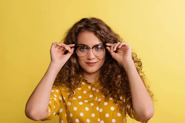 Portréja egy fiatal nő szemüveg egy stúdióban a sárga háttér. — Stock Fotó