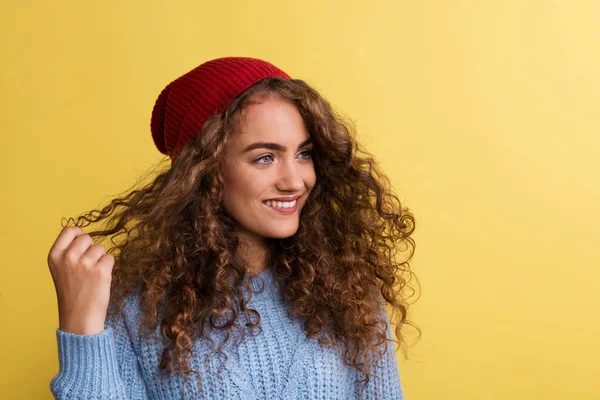 Portret van een jonge vrouw met wollen hoed in een studio op een gele achtergrond. — Stockfoto