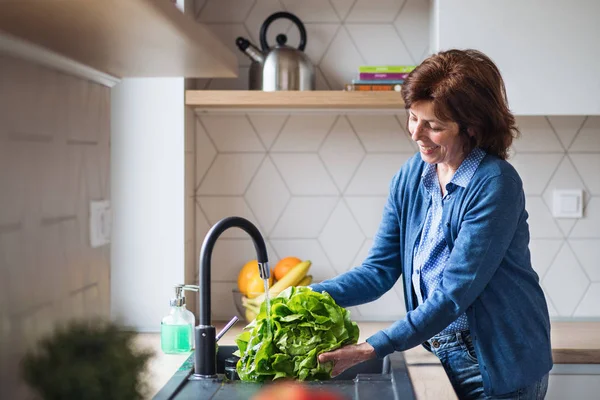 A portrait of senior woman indoors at home, washing lettuce. — Stock Photo, Image