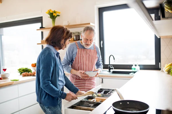 A portrait of senior couple in love indoors at home, cooking. — Stock Photo, Image