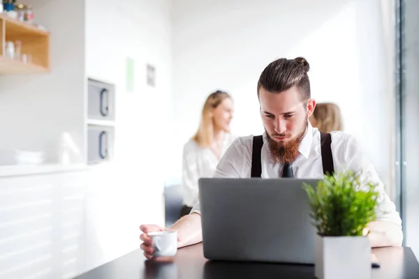 Ett porträtt av ung affärsman med dator på ett kontor, som arbetar. — Stockfoto