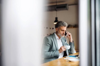 Bir kafede masada kahve ve akıllı telefon ile Olgun adam.
