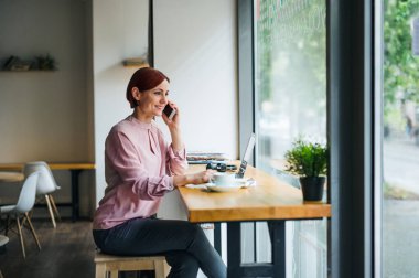 Kahveve telefon la bir kafede masada oturan bir kadın, bir telefon görüşmesi yapıyor.
