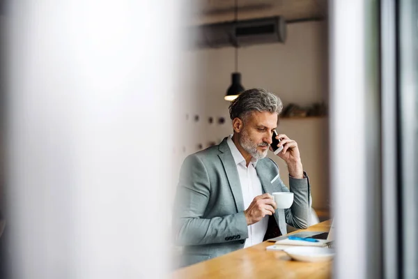 Hombre maduro con café y teléfono inteligente en la mesa en un café . —  Fotos de Stock