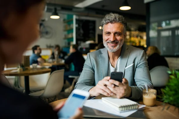 Homme et femme ayant une réunion d'affaires dans un café, en utilisant des smartphones . — Photo