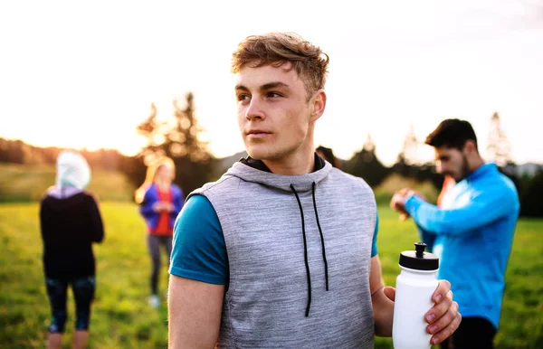 Un retrato de un joven con un gran grupo de personas haciendo ejercicio en la naturaleza . —  Fotos de Stock