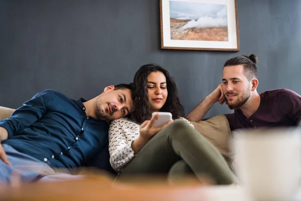 Un grupo de jóvenes amigos con teléfono inteligente sentado en el sofá en el interior, concepto de compartir casa . — Foto de Stock