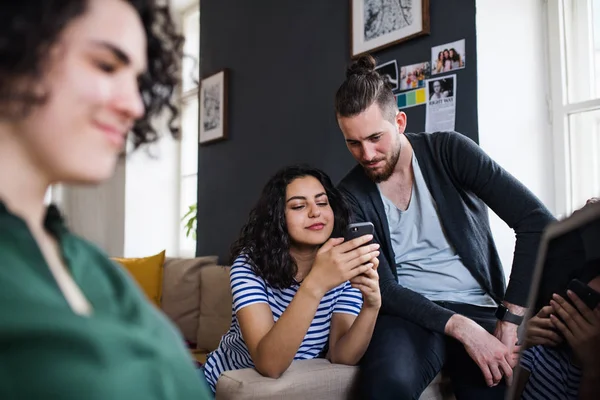 Un gruppo di giovani amici con smartphone seduti sul divano in casa, concetto di condivisione della casa . — Foto Stock