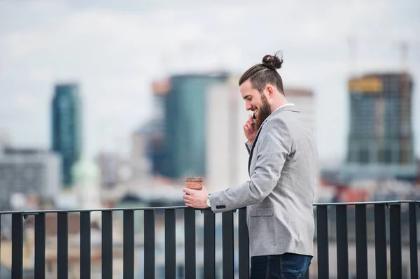 Un jeune homme d'affaires avec smartphone debout sur une terrasse, faisant un appel téléphonique . — Photo