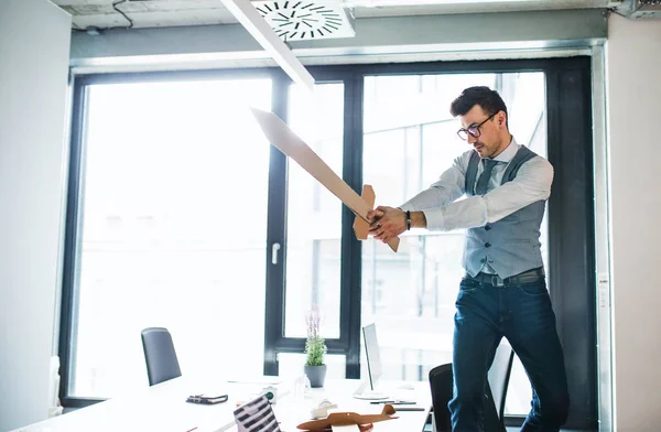 En ung affärsman med svärd på ett kontor, ha kul. Ett konkurrens koncept. — Stockfoto