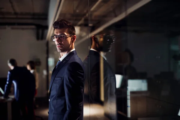 Un ritratto di un giovane uomo d'affari in piedi in un ufficio la sera . — Foto Stock