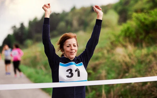 Corredora senior que cruza la línea de meta en una competición de carreras en la naturaleza . — Foto de Stock