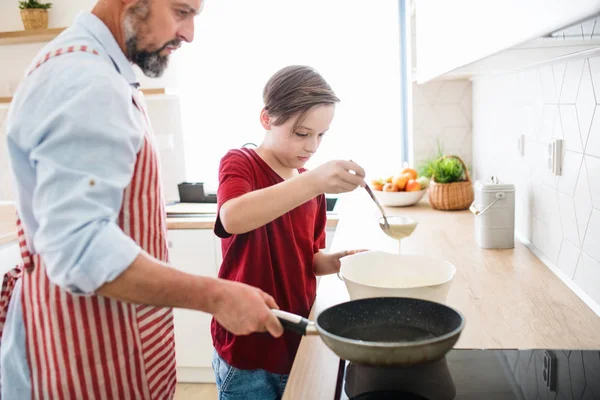 Зрелый отец с маленьким сыном в помещении на кухне, печет блинчики . — стоковое фото