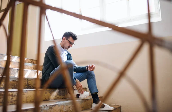 A young man sitting indoors on staircase. — Stock Photo, Image