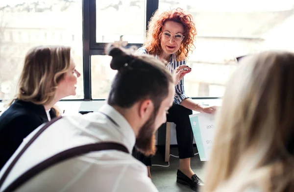 A group of young business people sitting on the floor in an office, talking. — Stock Photo, Image