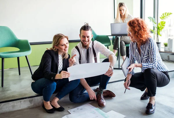 En grupp unga affärsfolk som sitter på golvet på ett kontor, pratar. — Stockfoto