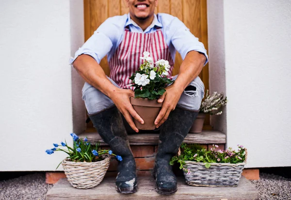 Unrecognizable young man gardener sitting in front of door at home. — Stock Photo, Image