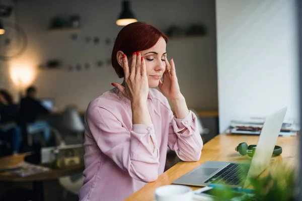 Una mujer con portátil sentada a la mesa en un café, sufriendo de dolor de cabeza . — Foto de Stock