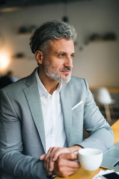 Mogen man med kaffe vid bordet i ett kafé, blickar ut ur fönstret. — Stockfoto