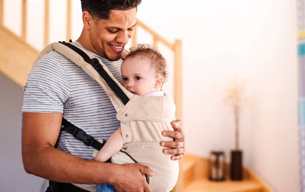 Un padre con un pequeño hijo en el portador en el interior de casa . — Foto de Stock