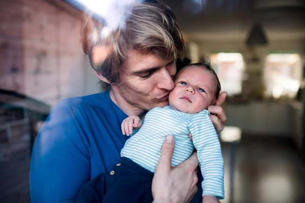 Un giovane padre che tiene in braccio un neonato a casa, baciandolo . — Foto Stock