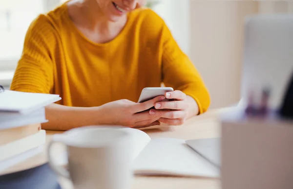 Une jeune étudiante assise à la table, utilisant smartpone lors de ses études . — Photo