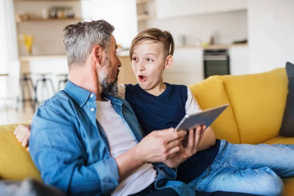 Ayah yang dewasa dengan anak kecil duduk di sofa di dalam ruangan, menggunakan tablet . — Stok Foto