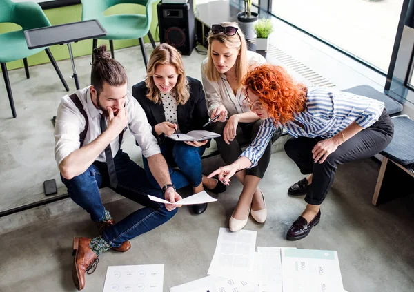 A group of young business people sitting on the floor in an office, talking. — Stock Photo, Image