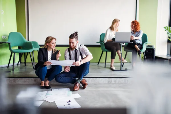 Un groupe de jeunes gens d'affaires assis par terre dans un bureau, parlant . — Photo