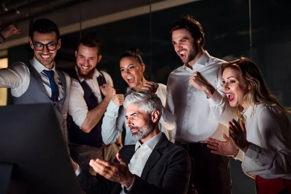 Un grupo de empresarios en una oficina por la noche, expresando emoción . — Foto de Stock