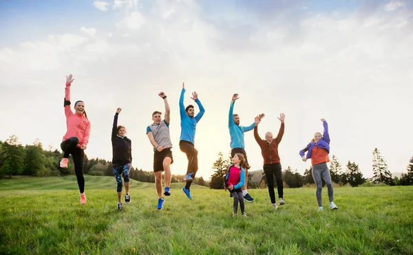 Un grande gruppo di sportivi di più generazioni in piedi nella natura, saltando . — Foto Stock