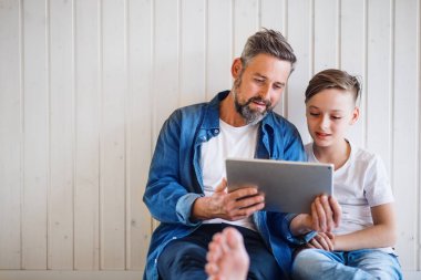 Küçük oğlu ile olgun baba kapalı oturan, tablet kullanarak. Kopyalama alanı.
