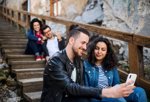 Um grupo de jovens amigos sentados ao ar livre na escadaria da cidade, tomando selfie . — Fotografia de Stock