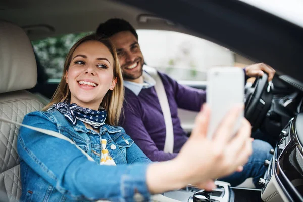 Happy young couple with smartphone sitting in car, taking selfie. — Stock Photo, Image