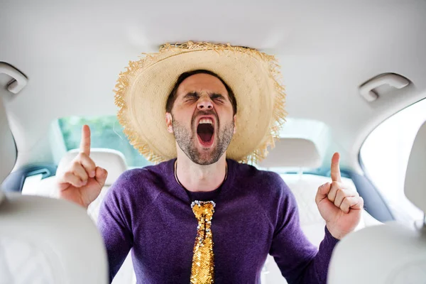 Uomo allegro con accessori per feste seduto in auto, divertendosi . — Foto Stock