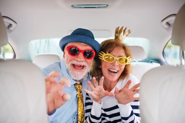 Coppia anziana allegra con accessori per feste seduti in auto, divertendosi . — Foto Stock