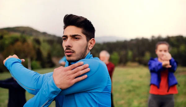 A portrait of young man with large group of people doing exercise in nature. — Stock Photo, Image