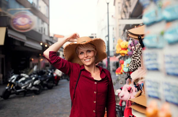 Mladá žena stojící venku ve městě na dovolené, zkouší klobouk. — Stock fotografie