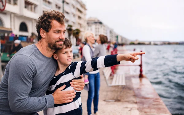 Padre con piccolo figlio in piedi all'aperto in città in riva al mare, parlando . — Foto Stock