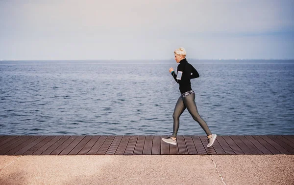 Vista laterale della giovane sportiva che corre all'aperto sulla spiaggia . — Foto Stock