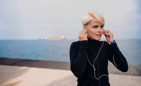 Porträt einer jungen Sportlerin mit Kopfhörern, die draußen am Strand steht. — Stockfoto