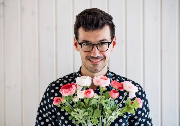 Jovem com flores de pé contra parede de fundo de madeira branca . — Fotografia de Stock