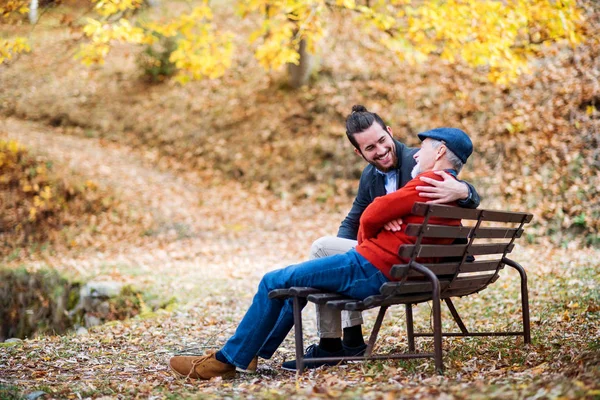 Senior far och hans son sitter på bänken vid sjön i naturen, talar. — Stockfoto