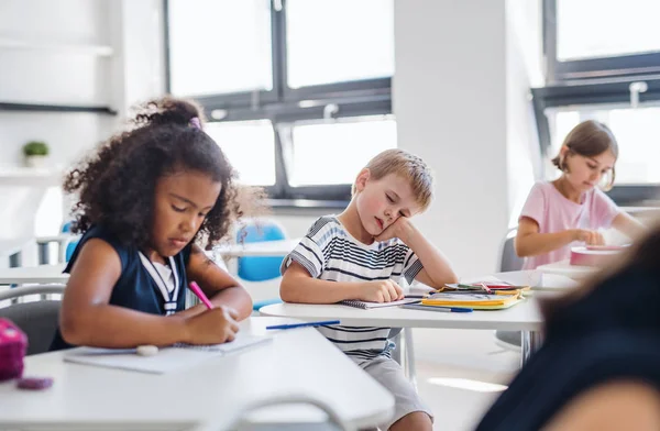 Um pequeno menino da escola cansado sentado na mesa em sala de aula, dormindo . — Fotografia de Stock